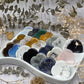 A collection of heart shaped worry stones in various colors and stones displayed in a white dish.
