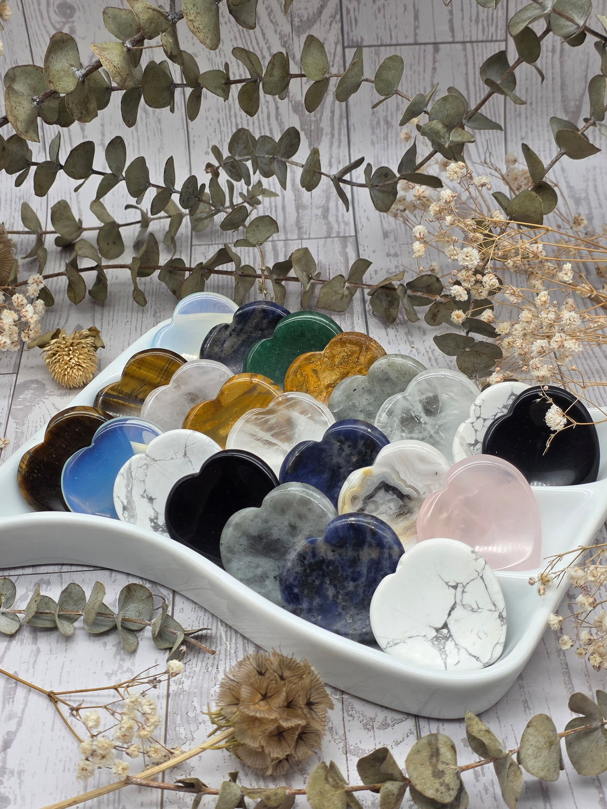 A collection of heart shaped worry stones in various colors and stones displayed in a white dish.