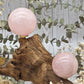 Medium polished rose quartz sphere on a wooden stand with decorative foliage.