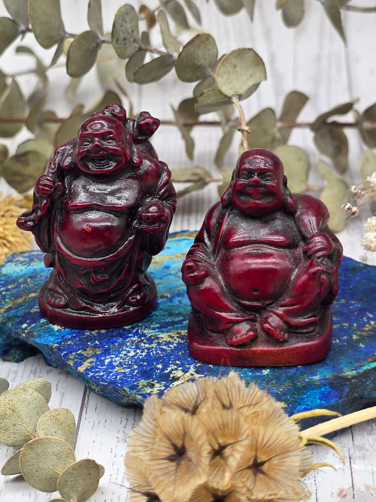 Dark red resin Buddha figurine on a blue stone with foliage