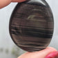 A polished Midnight Lace Obsidian palm stone held between fingers