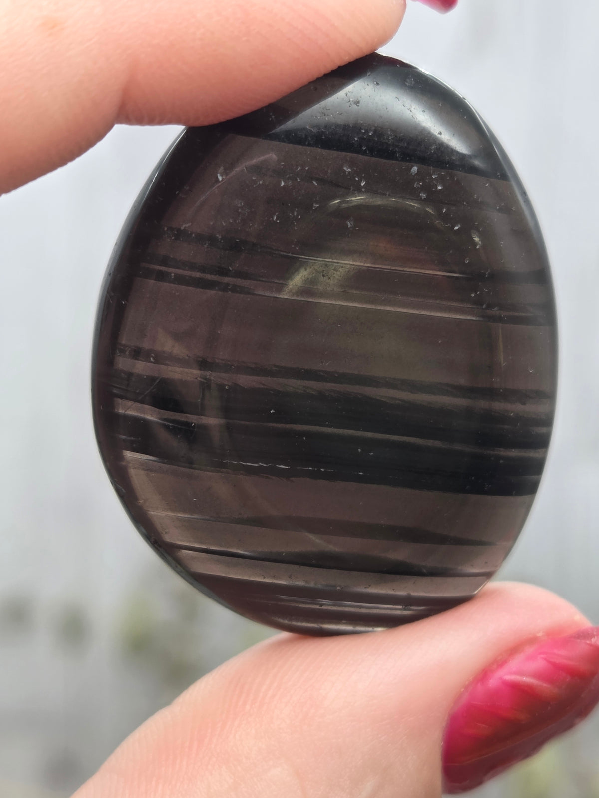 A polished Midnight Lace Obsidian palm stone held between fingers