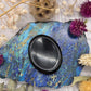 Polished black obsidian palm stone on a colorful background with dried flowers