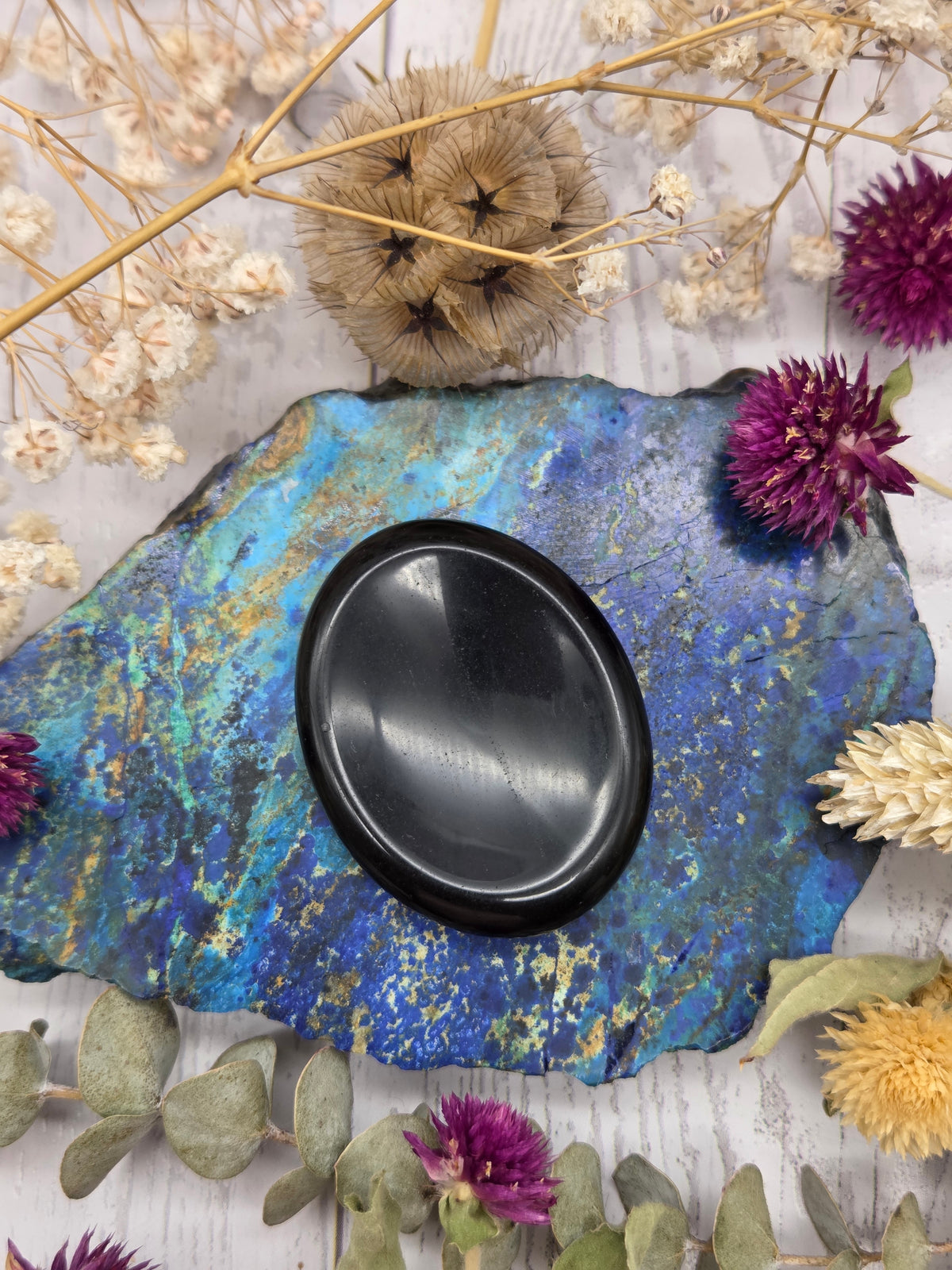 Polished black obsidian palm stone on a colorful background with dried flowers
