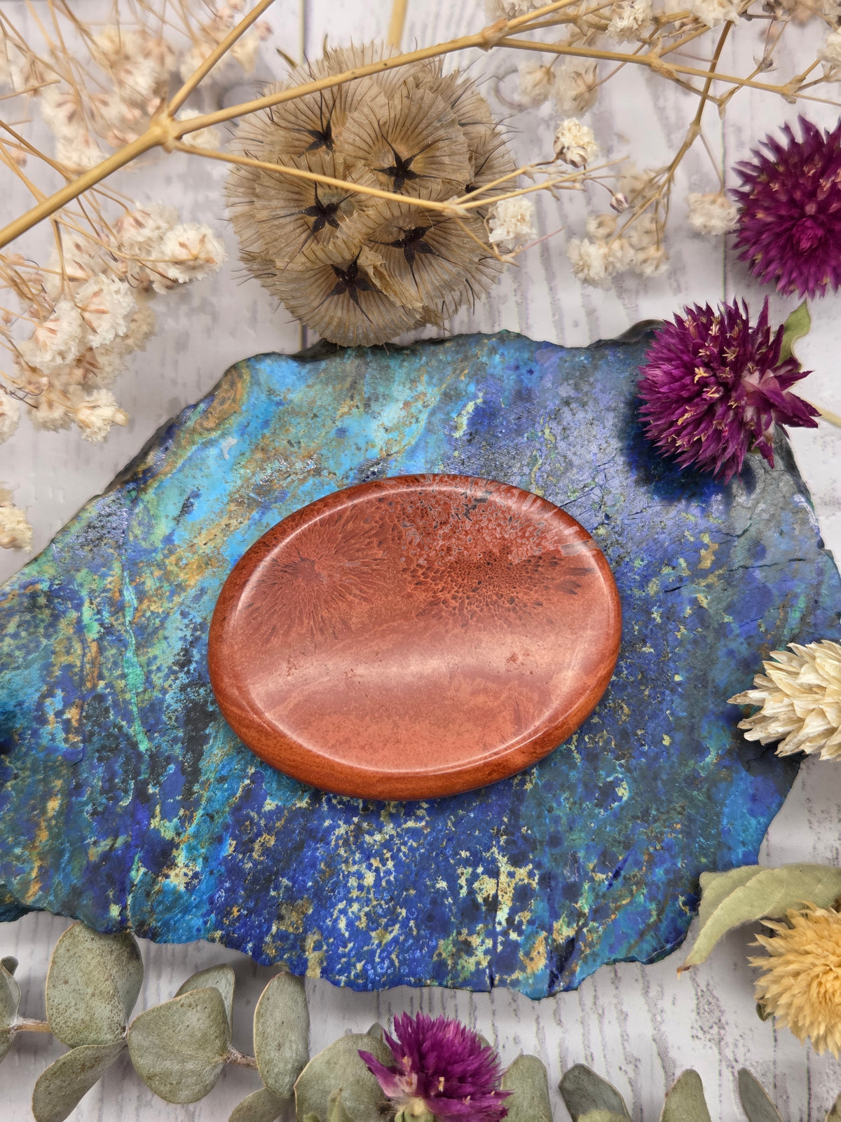 Polished Red Jasper worry stone on a colorful background with dried flowers