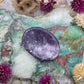A polished purple Lepidolite worry stone on a colorful background with dried flowers.