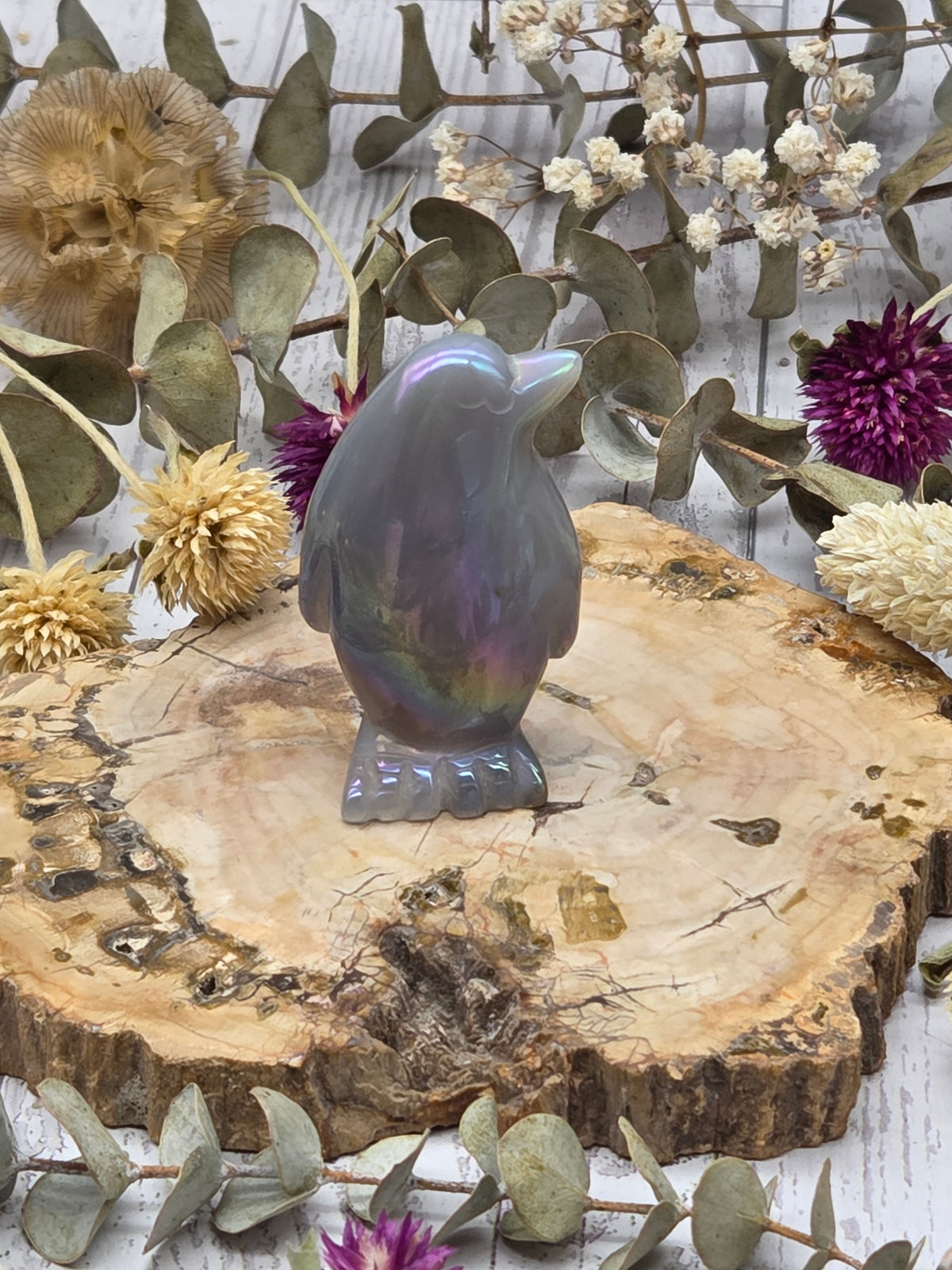 Iridescent aura agate penguin figurine on a wooden base with dried flowers