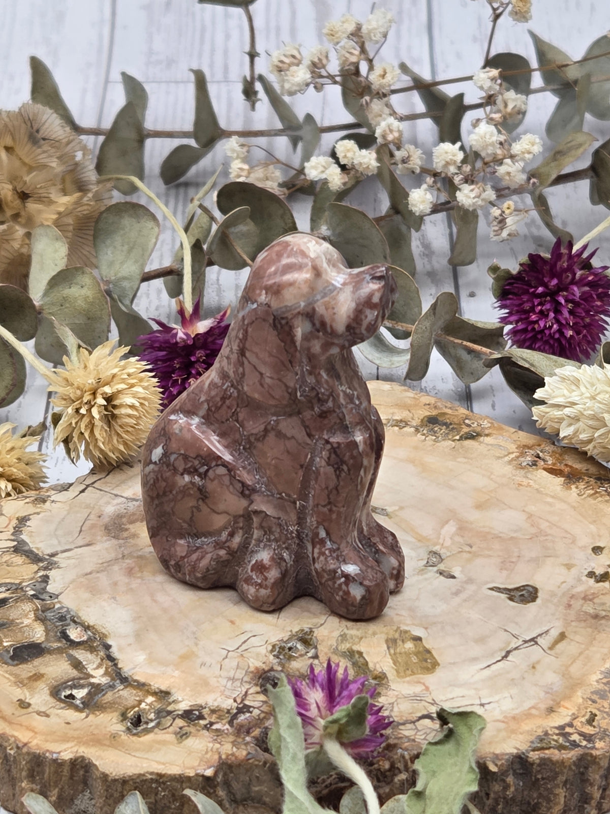 Strawberry Onyx dog carving on a wooden base surrounded by dried flowers