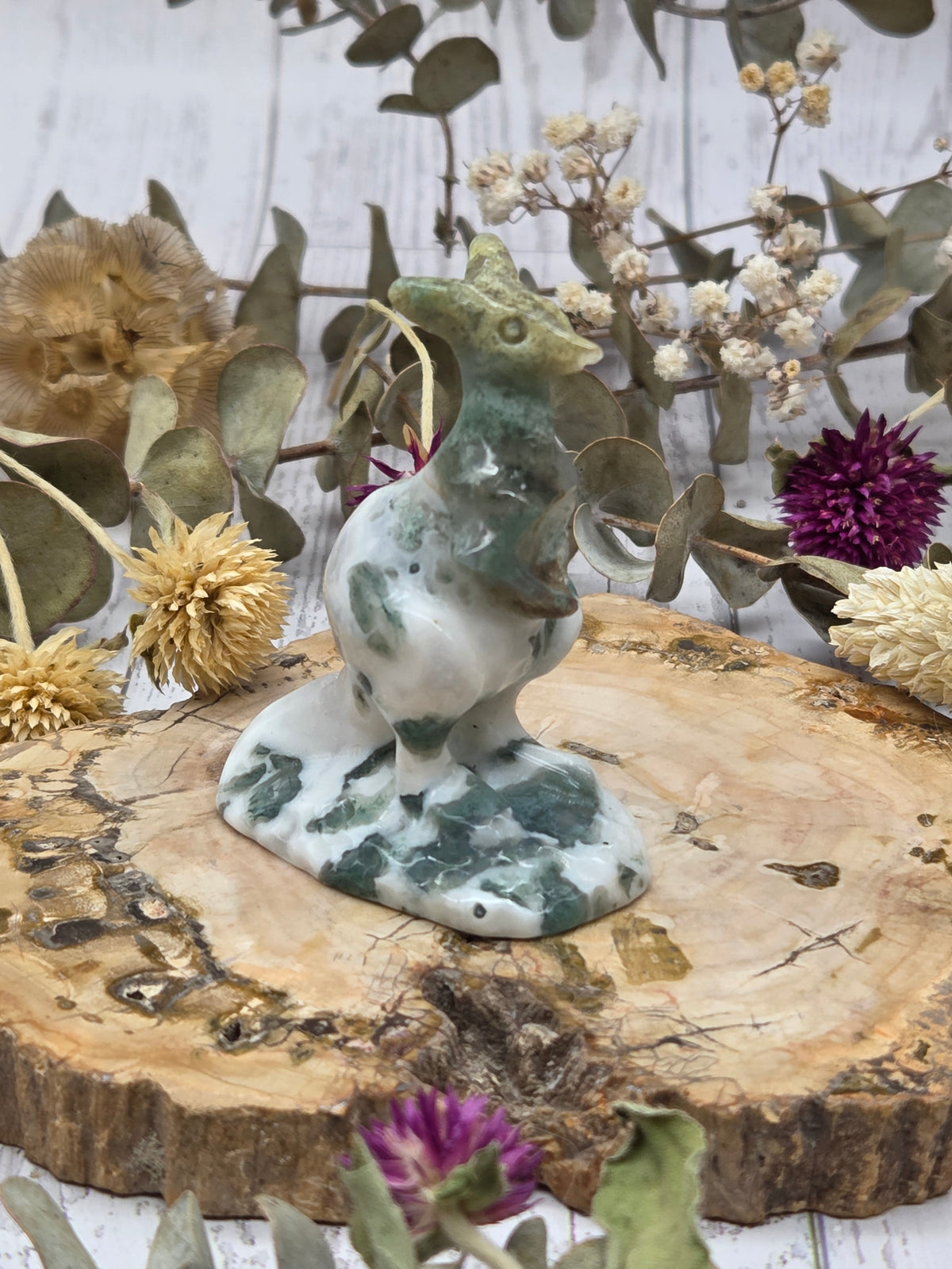 Moss agate kangaroo carving on a wooden base surrounded by dried flowers