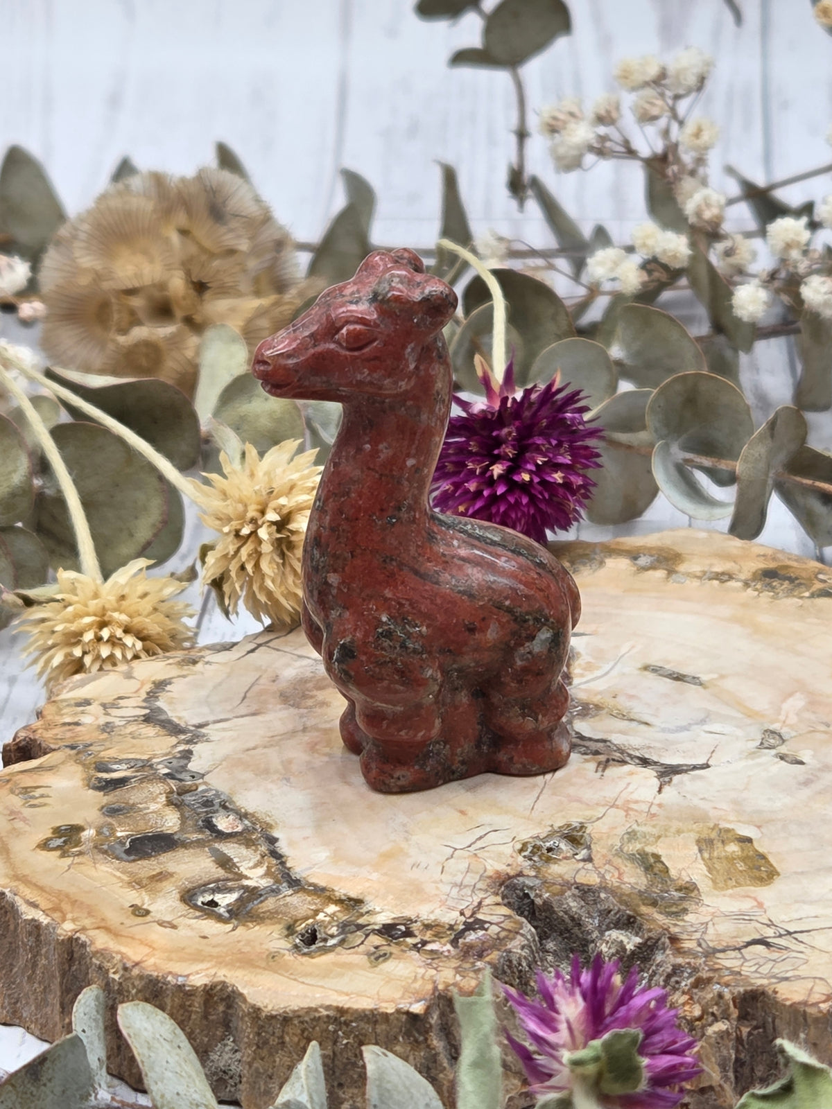 Red Jasper giraffe figurine on a wooden base with dried flowers