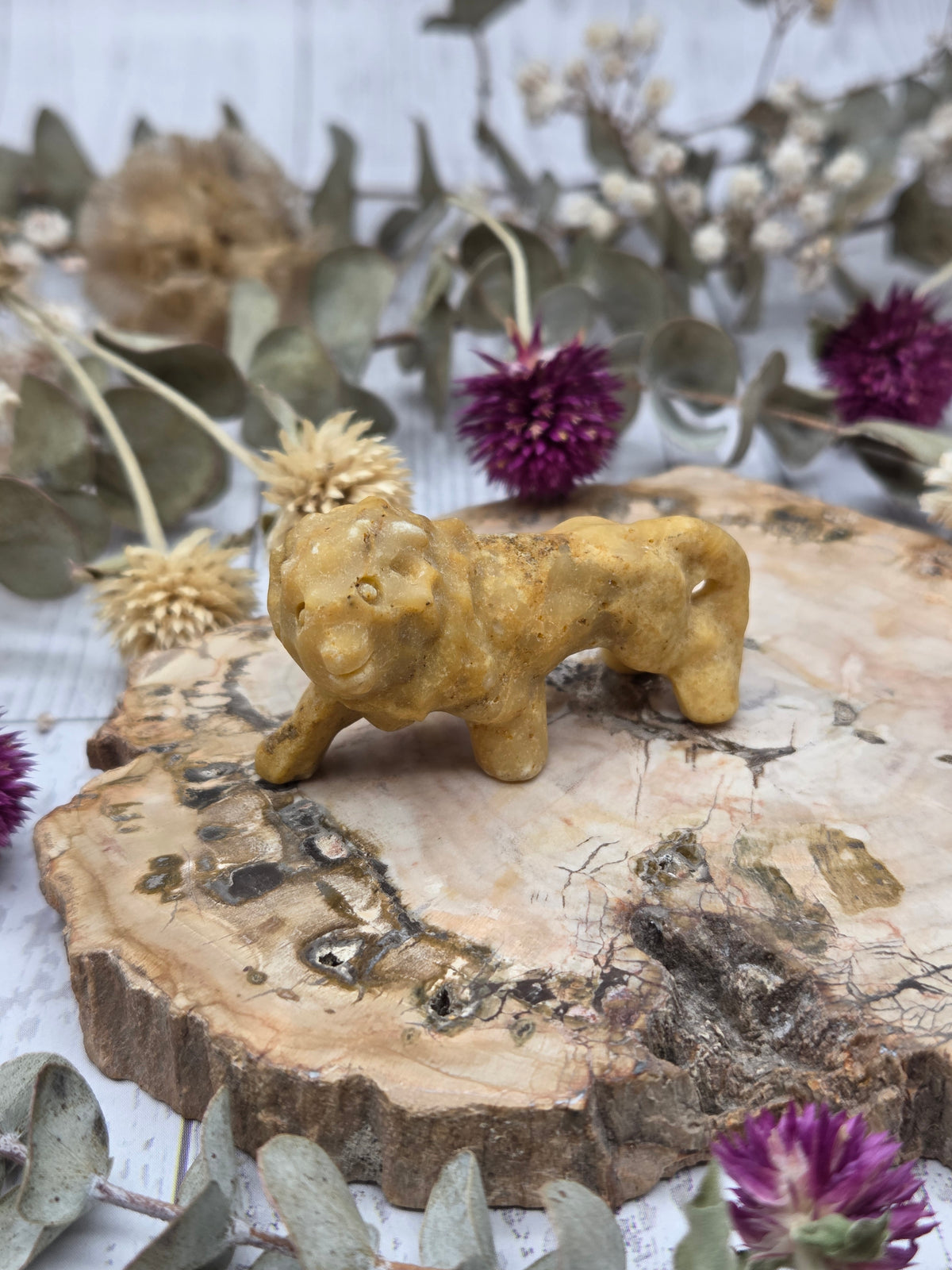 Yellow Aventurine lion carving on a wooden base with dried flowers in the background