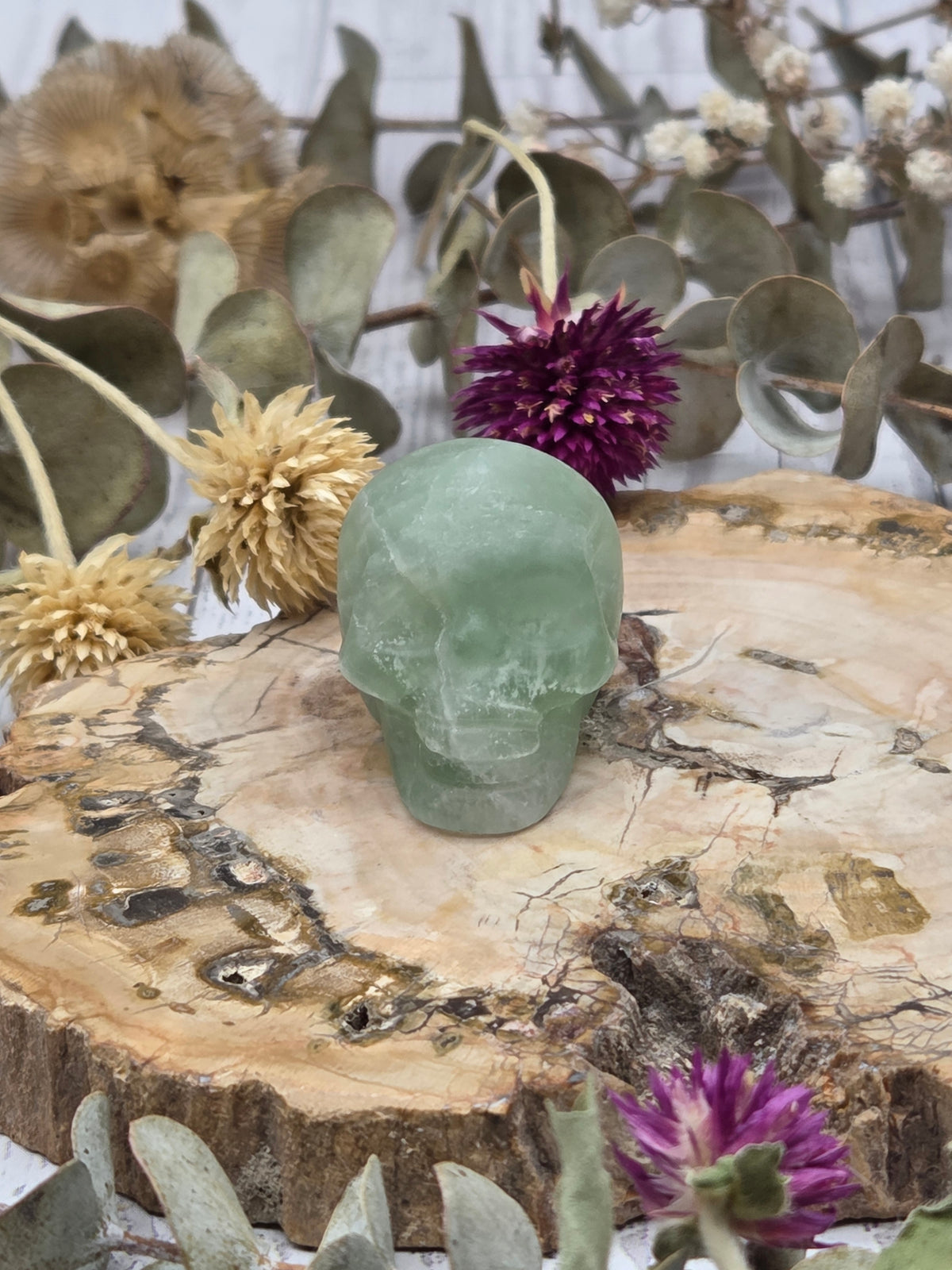 Green fluorite skull on a wooden slab with dried flowers