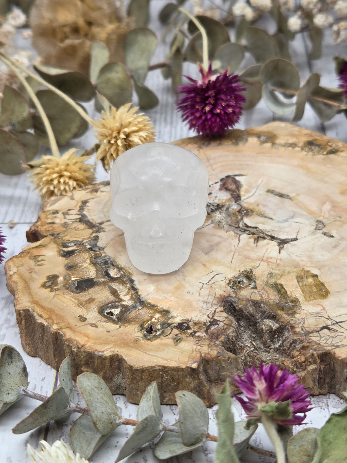 Clear quartz skull on a wooden base surrounded by dried flowers