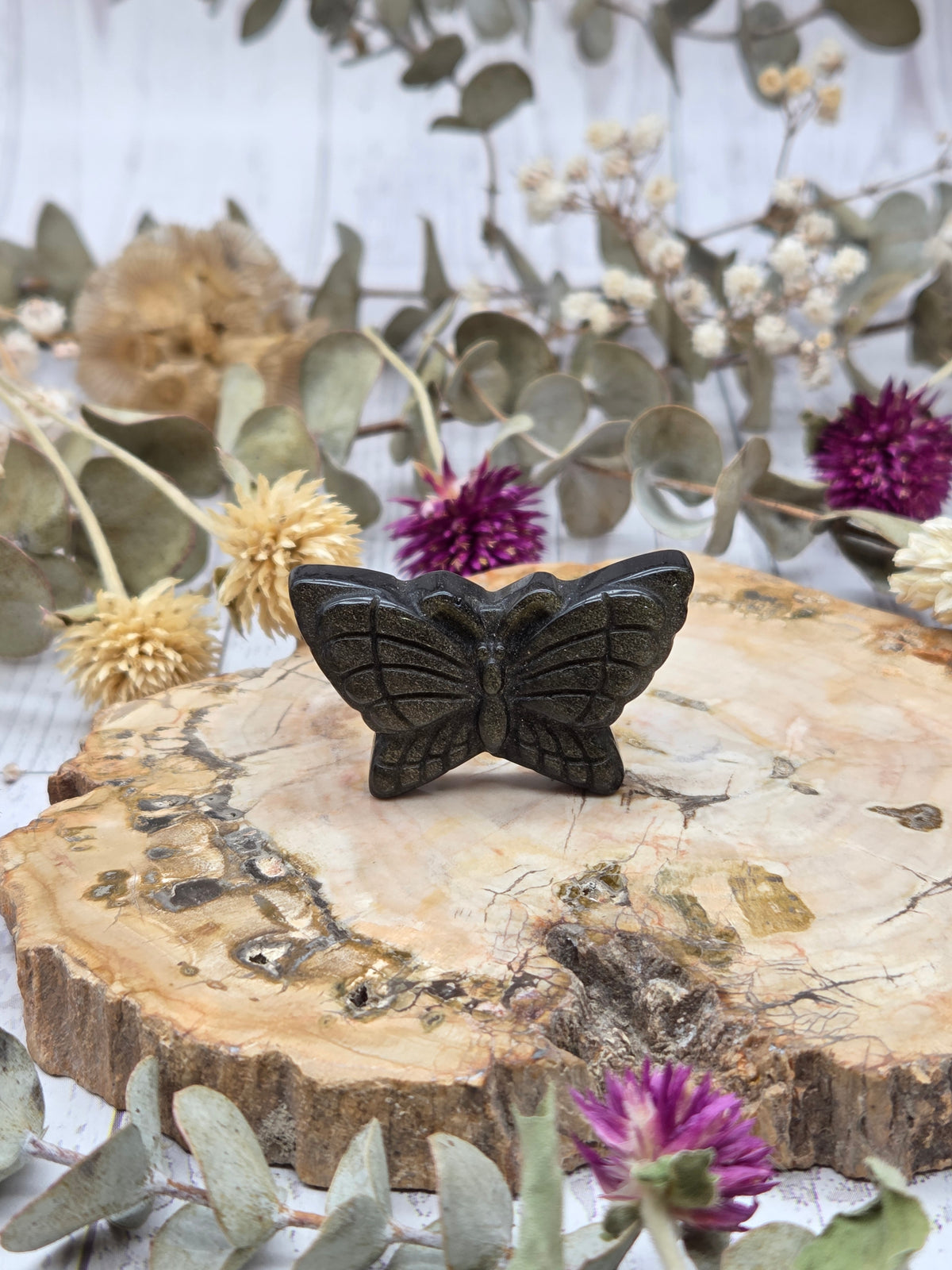 Golden sheen obsidian butterfly carving on a wooden slab with dried flowers