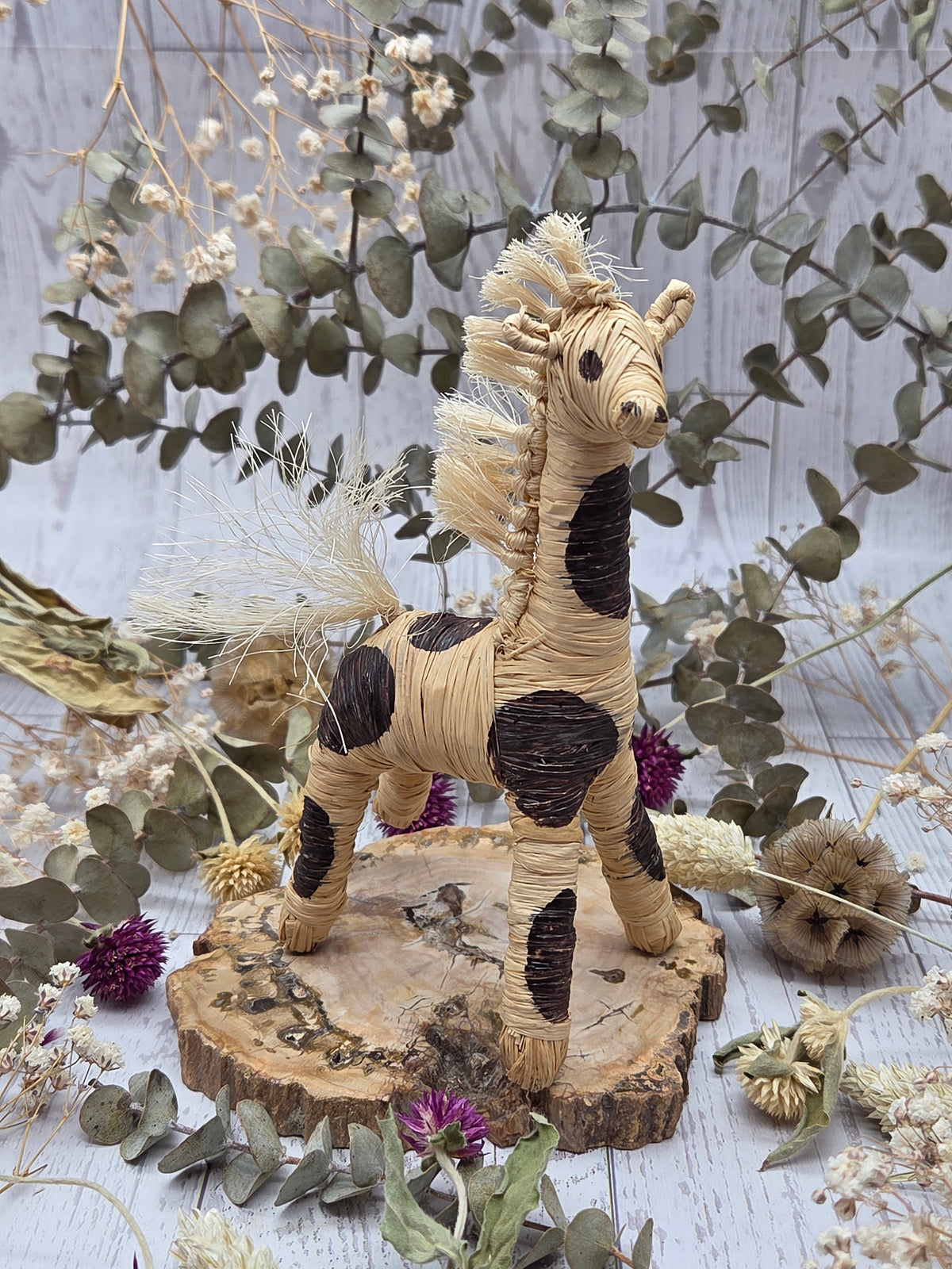 Banana fiber giraffe figurine on a wooden base with dried flowers