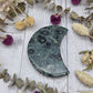 Kambaba Jasper moon carving on a wooden surface surrounded by dried flowers