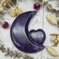 A polished rainbow fluorite carving in the shape of a moon with a heart