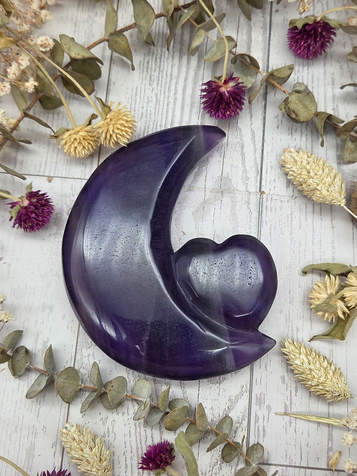 A polished rainbow fluorite carving in the shape of a moon with a heart