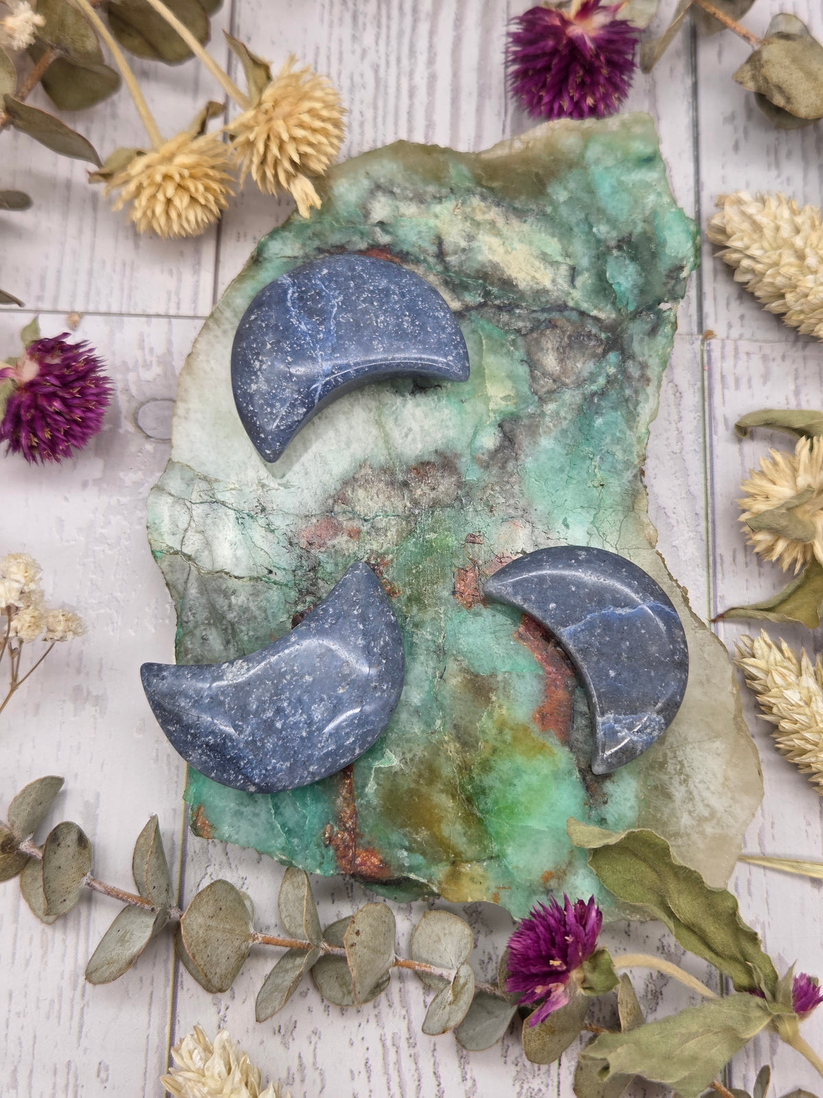 Blue Dumortierite moon carving on a colorful background with dried flowers