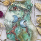 Two aquamarine moon carvings on a colorful stone background
