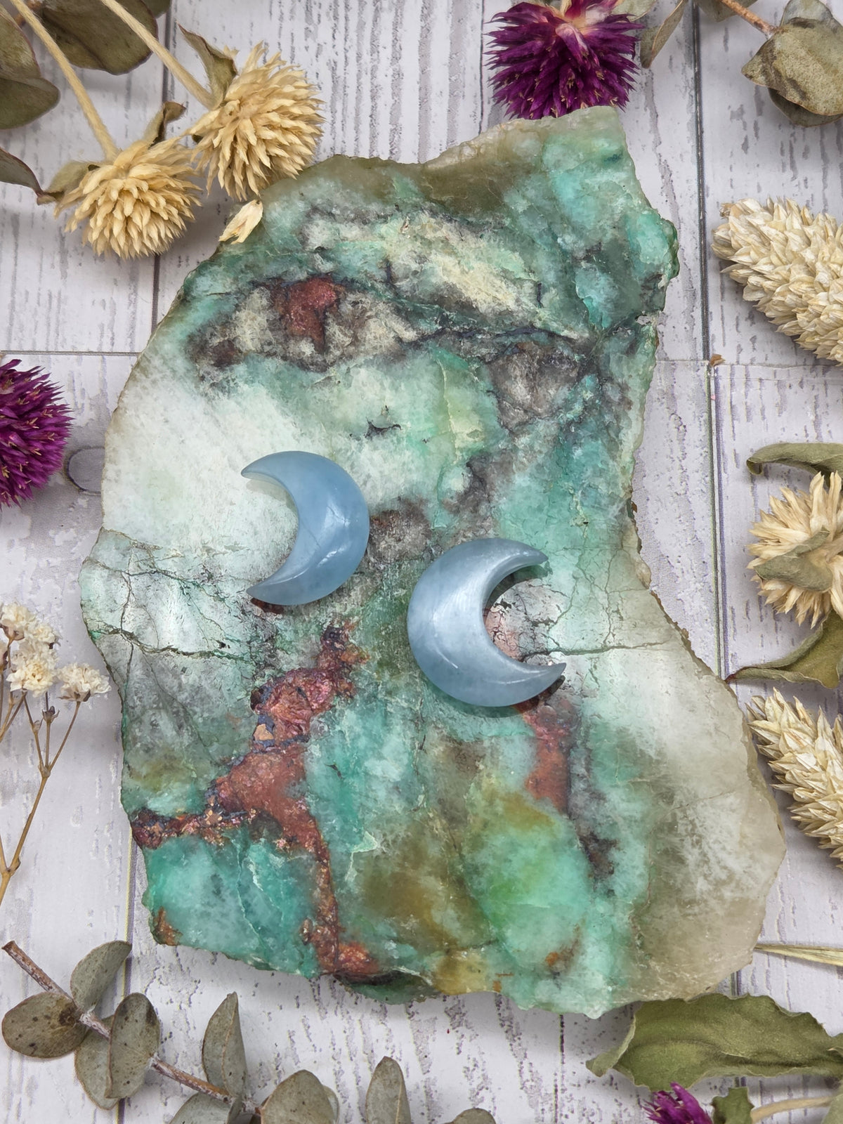 Two aquamarine moon carvings on a colorful stone background