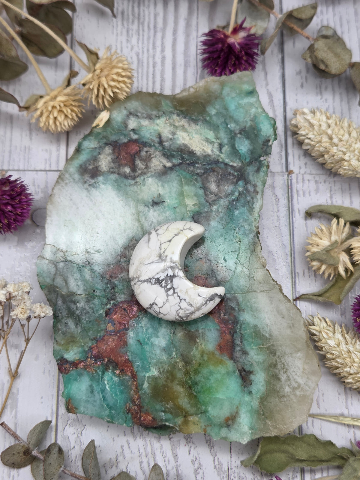 A small polished howlite moon carving on a colorful stone background